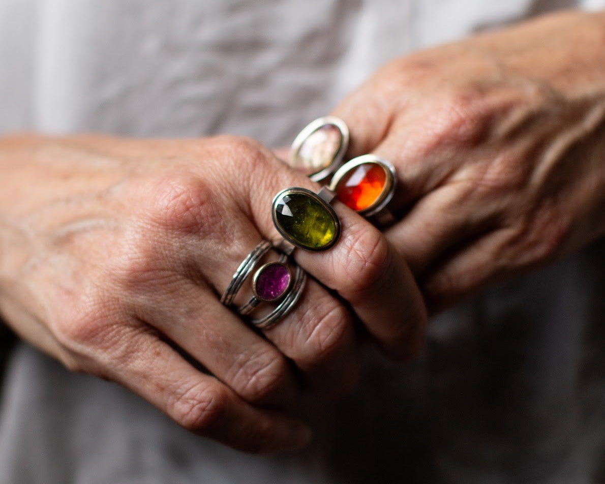 Close-up of a hand wearing multiple rings with colorful gemstones on a neutral background